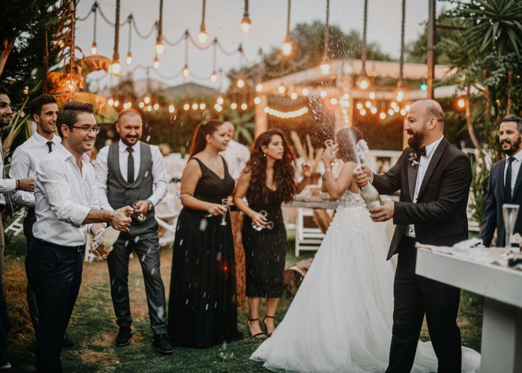 pexels-photo-6119578-6119578 Joyful wedding party celebration outdoors with champagne and smiling guests dressed in formal attire.